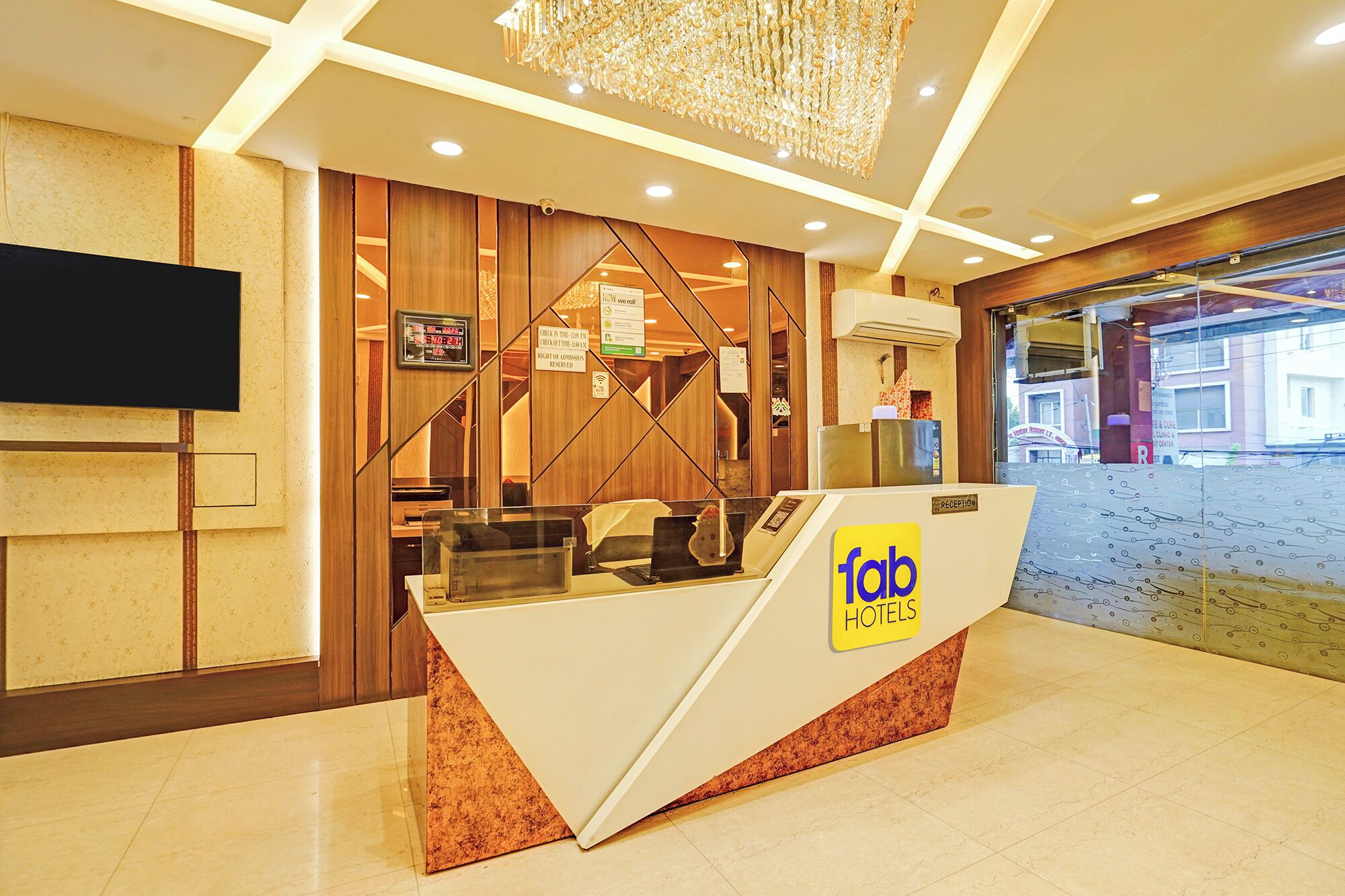 A hotel reception desk with a digital clock, a reception sign, and a view of the street outside.