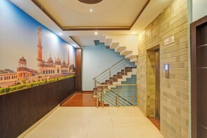 A hallway with a mural of a historical building, a staircase with a handrail, and an elevator. - Fabhotel Resto (Lucknow)