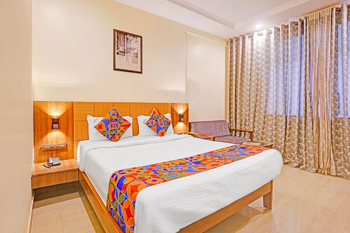 A hotel room with a wooden headboard, a bed with colorful bedding, a nightstand with a phone, and a window with curtains.