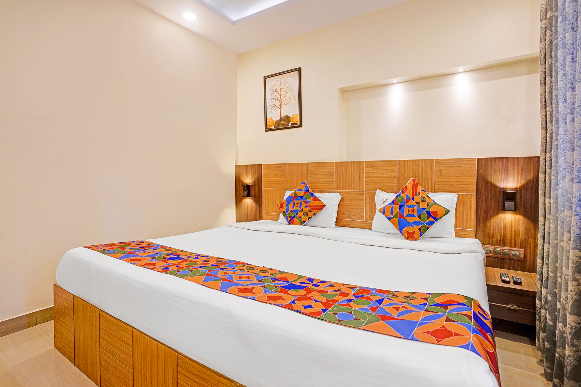 Habitación de hotel con cama, cabecera, mesita de noche y lámpara de pared.