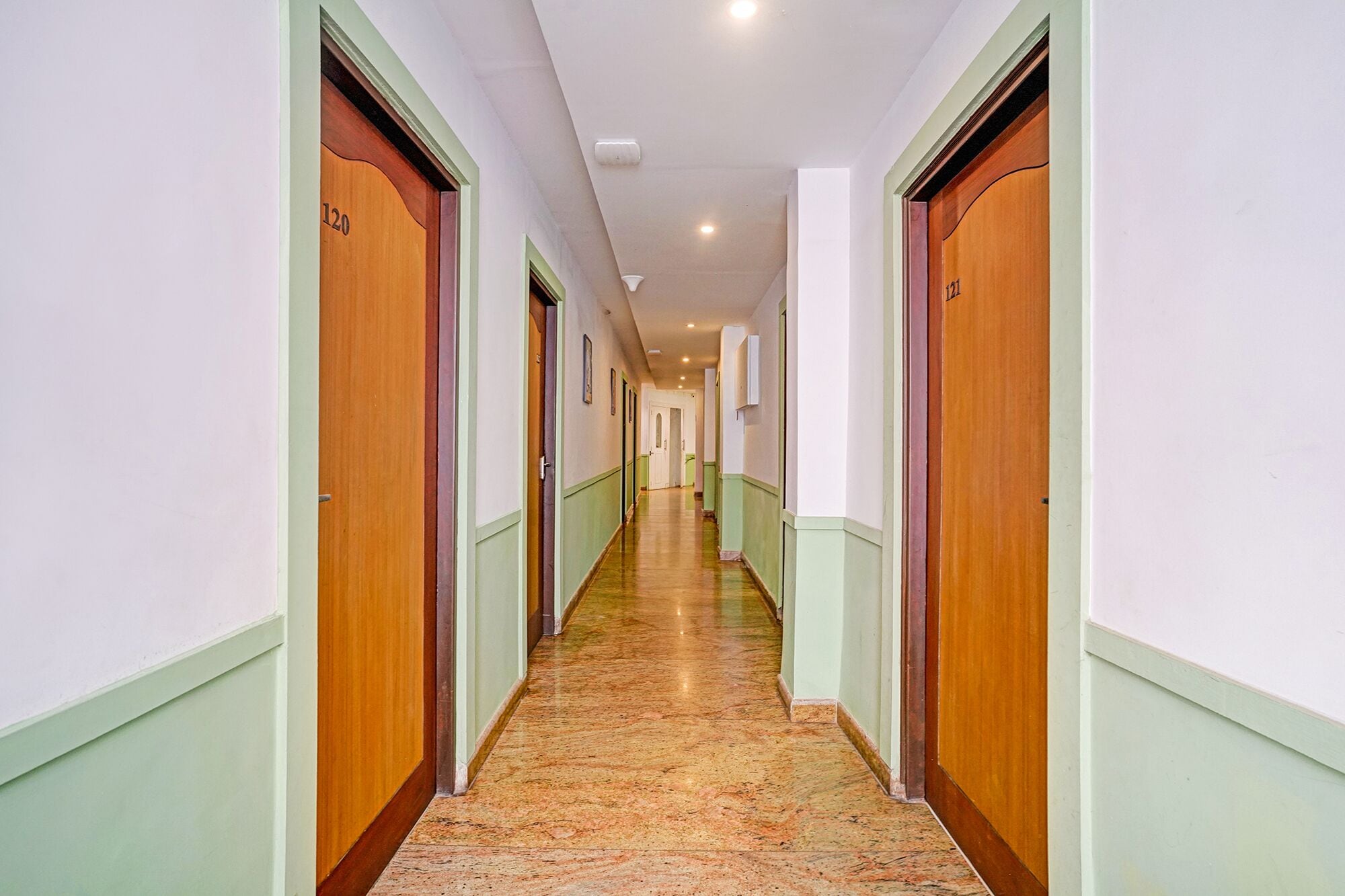 A hotel corridor with wooden doors, green trim, and a marble floor.