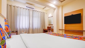 A hotel room with a bed, a desk, a chair, a TV mounted on the wall, and an air conditioning unit.