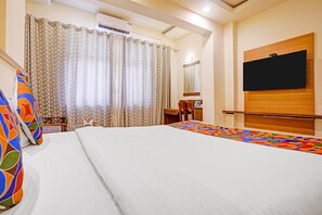 A hotel room with a bed, a desk, a chair, a TV mounted on the wall, and an air conditioning unit.