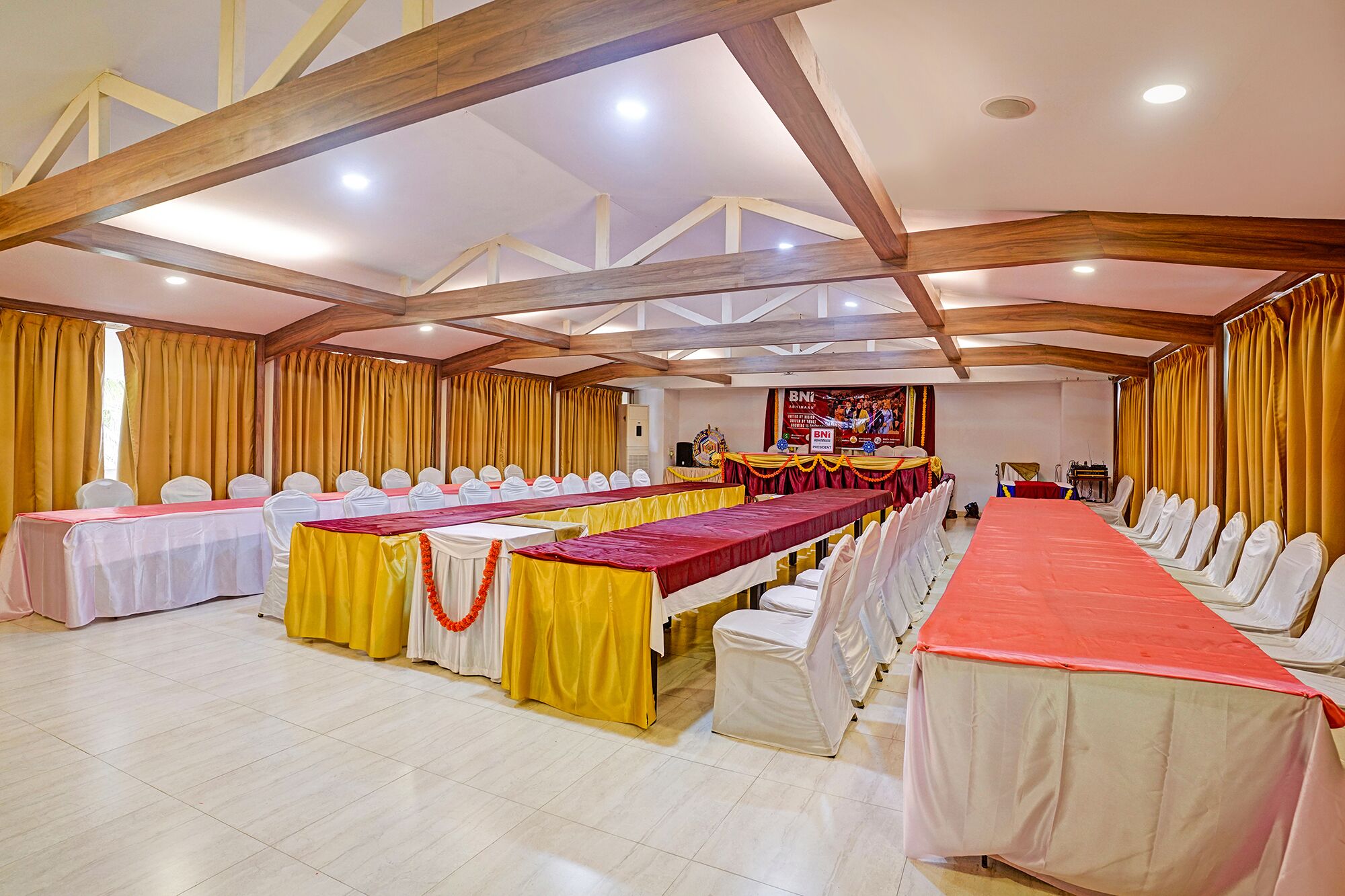 Un salón de conferencias con varias mesas, sillas blancas y cortinas amarillas.