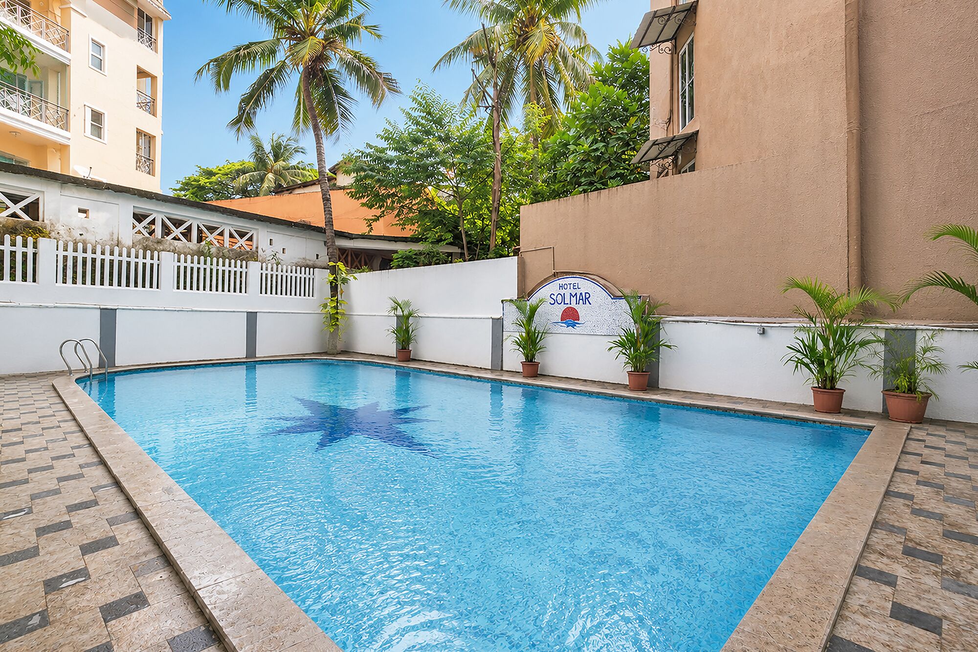 A swimming pool with a white fence, potted plants, and a sign for Hotel Solmar.