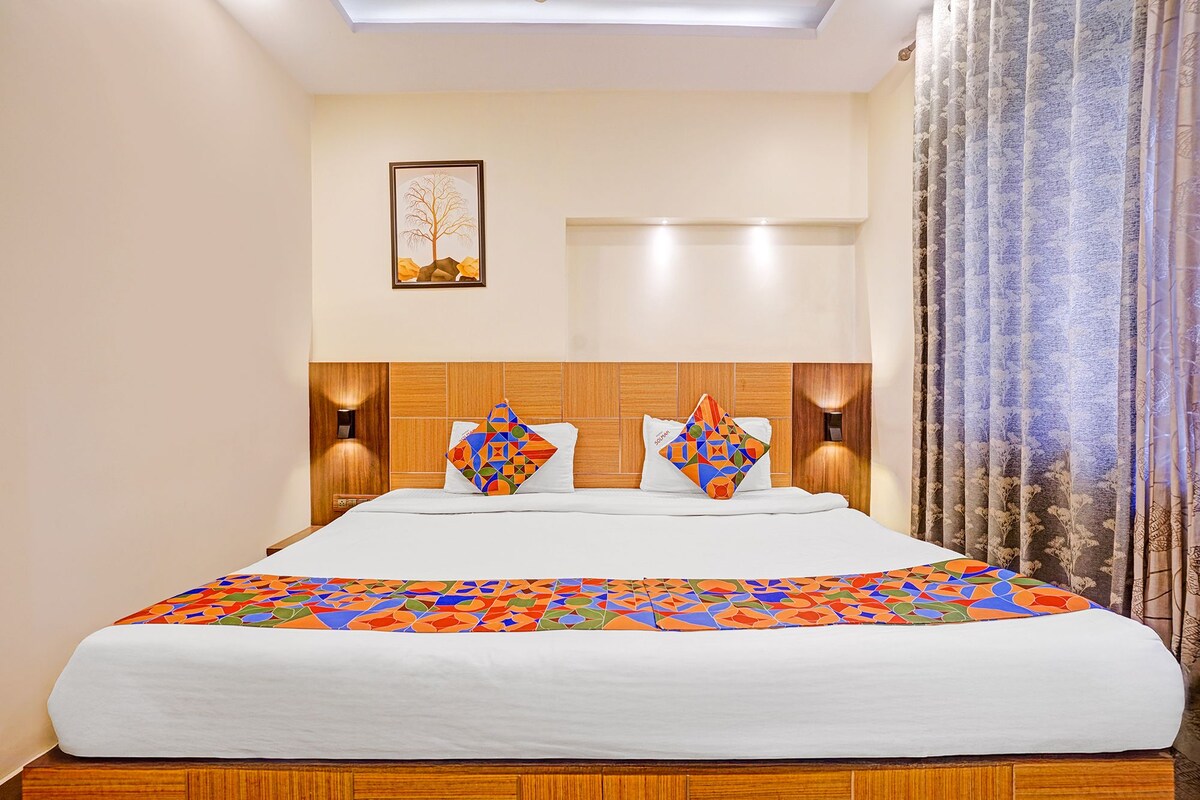 A hotel room with a large bed, two wall-mounted lamps, a framed picture on the wall, and a window with curtains.