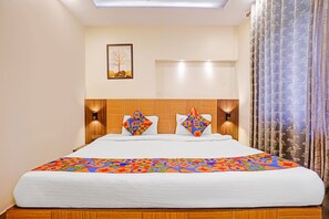 Ein Hotelzimmer mit einem großen Bett, zwei Wandlampen, einem gerahmten Bild an der Wand und einem Fenster mit Vorhängen.