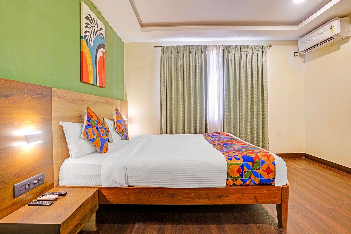 A hotel room with a wooden bed, a nightstand with a lamp, a painting on the wall, and a window with curtains.