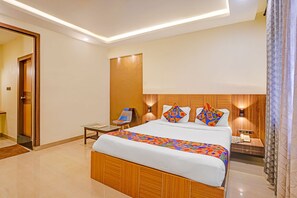 A hotel room with a wooden bed, a bedside table, a chair, and a nightstand with a phone. - Oriva Solmar (Panaji)