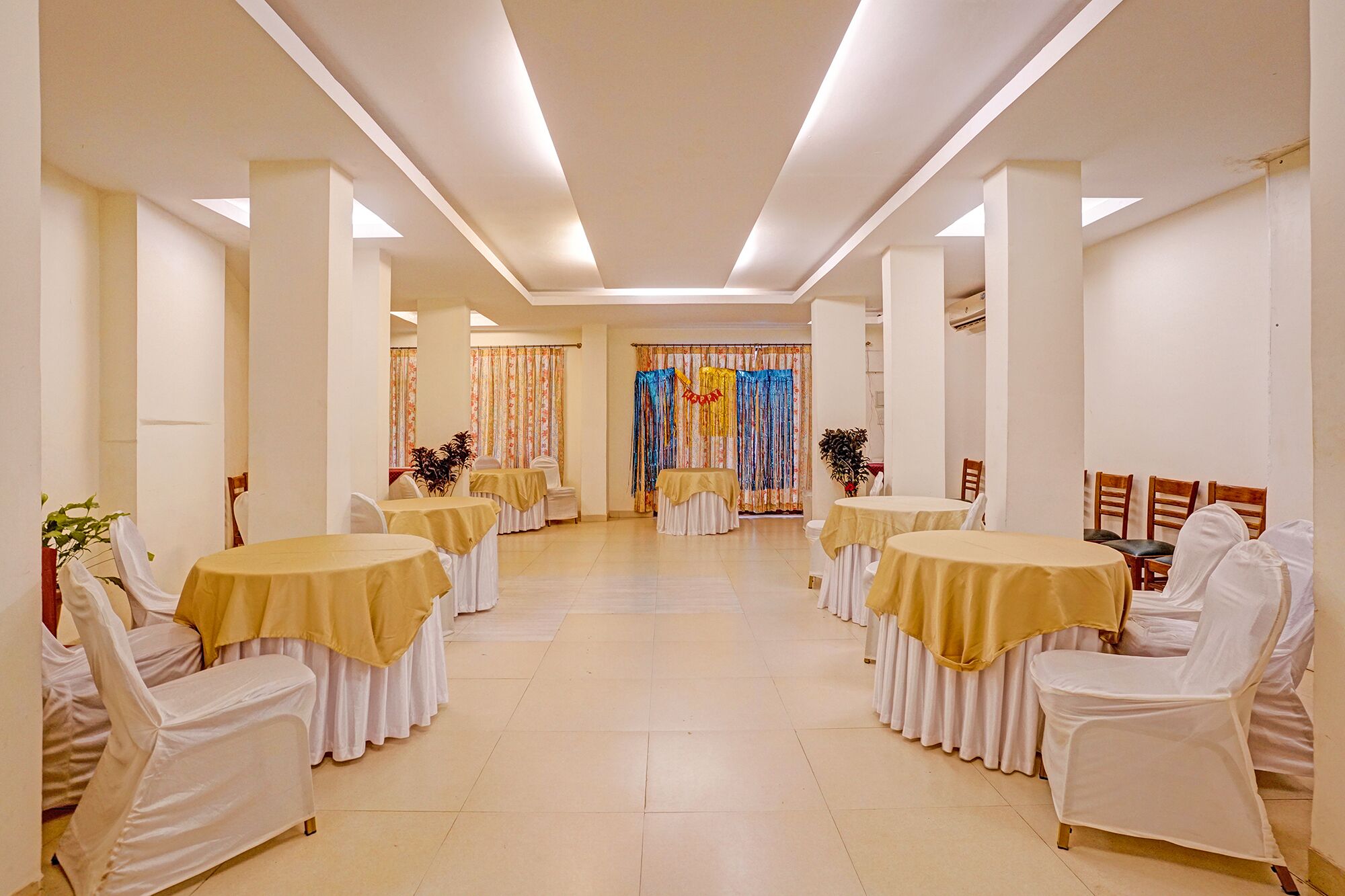 Un salón de banquetes con mesas redondas, sillas blancas y un pasillo central.