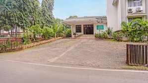 Un edificio con entrada pavimentada, rodeado de vegetación y una cerca de metal.