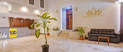 Vestíbulo de hotel con mostrador de recepción, una planta en maceta, un sofá y una pared con un logo.