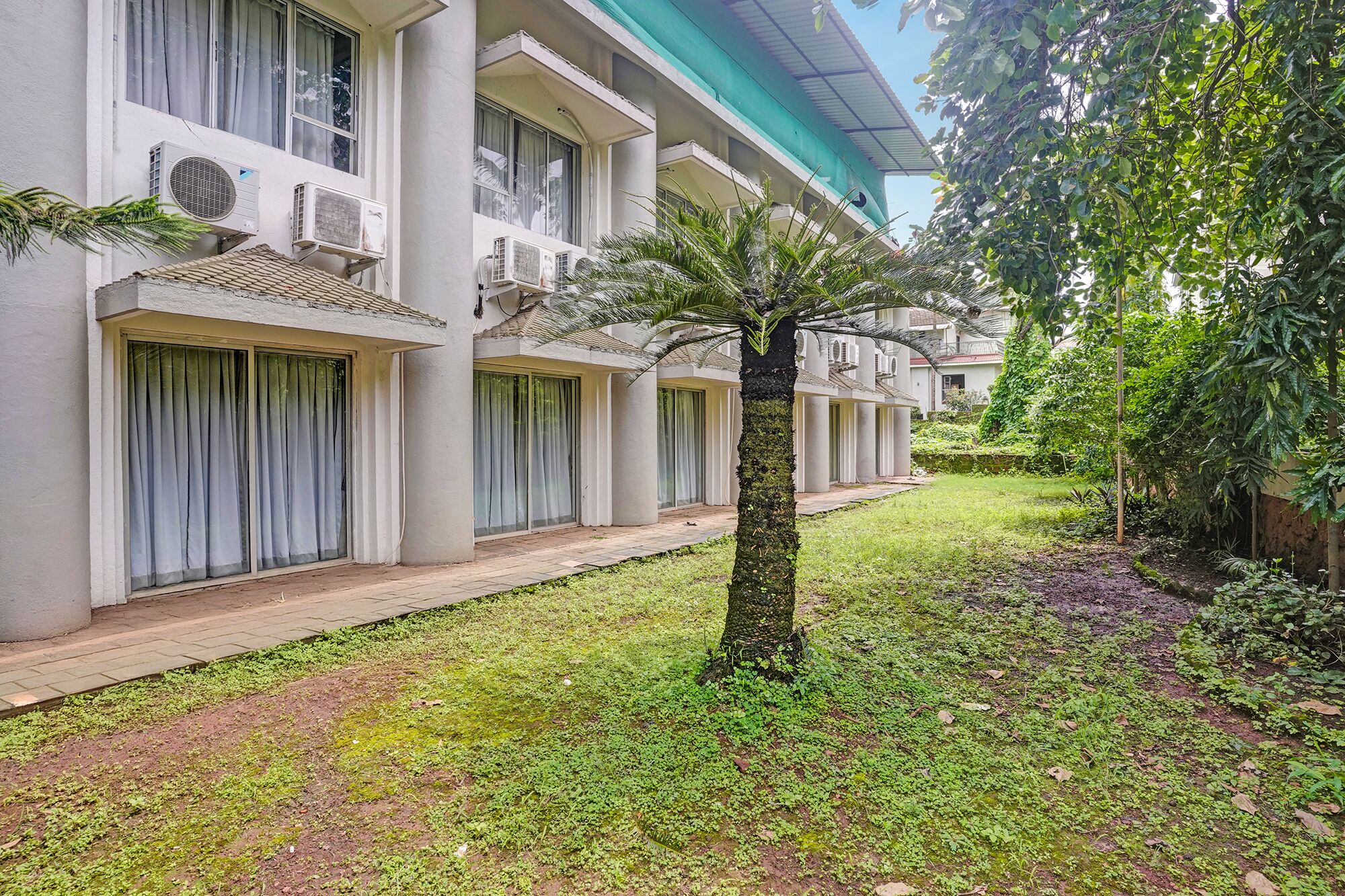 A hotel with multiple balconies, a central tree, and a well-maintained lawn.