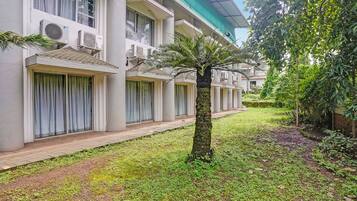 A hotel with multiple balconies, a central tree, and a well-maintained lawn.