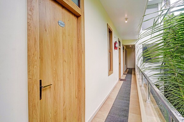 A corridor with wooden doors, a fire extinguisher, and a glass railing with greenery.
