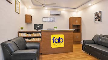 A reception desk with a logo, a computer, a bookshelf, and two leather sofas.