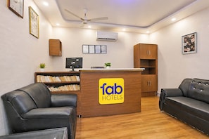 A reception desk with a logo, a computer, a bookshelf, and two leather sofas.
