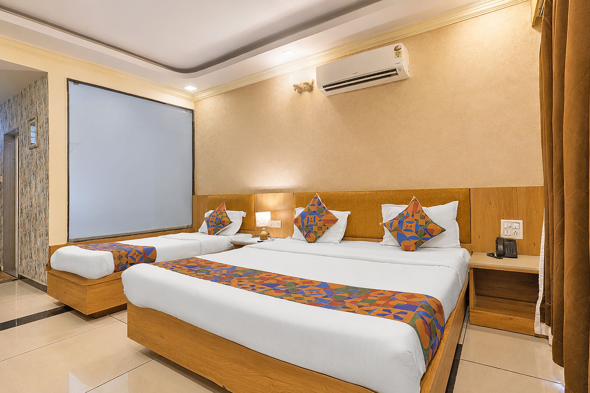 Quarto de hotel com uma cama grande, duas mesas de cabeceira, uma escrivaninha, um aparelho de ar condicionado e uma tela de projeção.