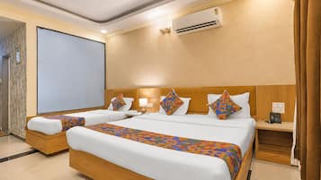 Habitación de hotel con una cama grande, dos mesitas de noche, un escritorio, un equipo de aire acondicionado y una pantalla para proyector.