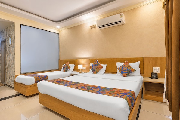 Habitación de hotel con una cama grande, dos mesitas de noche, un escritorio, un equipo de aire acondicionado y una pantalla para proyector.