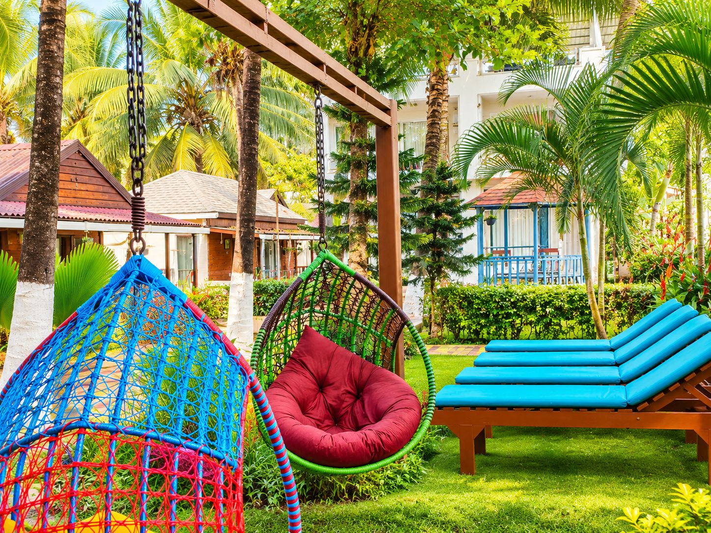 Un resort tropical con una hamaca, una silla roja acolchada y una silla de descanso azul.
