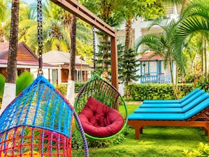 Un resort tropical con una hamaca, una silla roja acolchada y una silla de descanso azul.