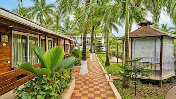 A pathway leading to a wooden building with a checkered floor, surrounded by lush greenery and palm trees.