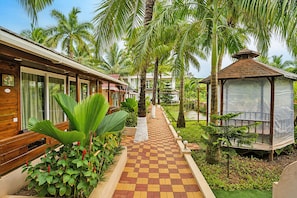 A pathway leading to a wooden building with a checkered floor, surrounded by lush greenery and palm trees.