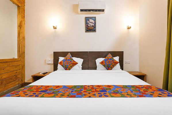 A hotel room with a bed, two nightstands, a wall-mounted air conditioner, and a framed picture above the bed.