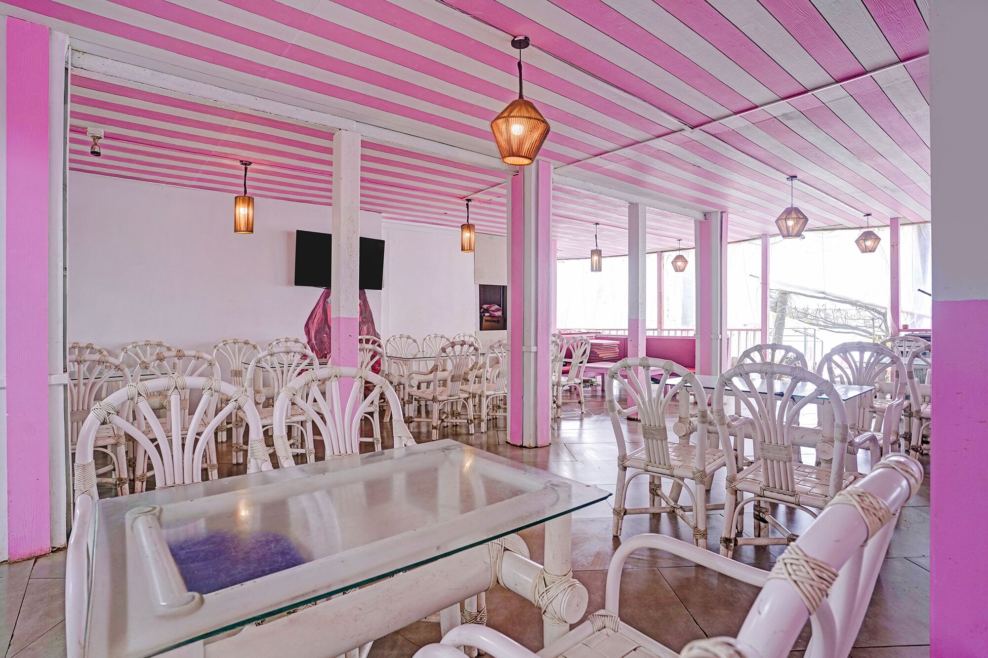 A room with white wicker furniture, pink and white striped ceiling, and hanging pendant lights.