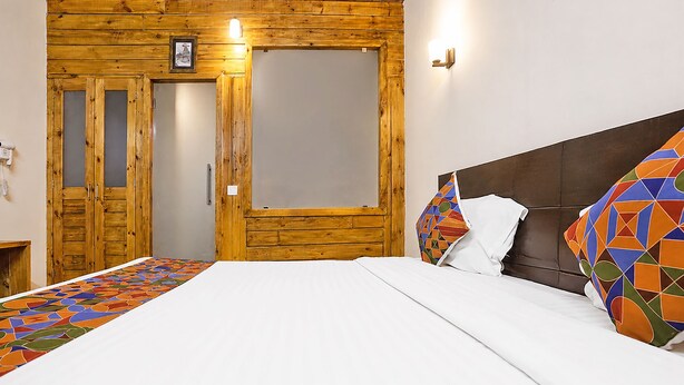 Un dormitorio con un armario de madera, una cama con almohadillas estampadas y una lámpara fijada a la pared.