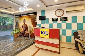 Ein Hotel-Rezeptionsbereich mit einer Buddha-Statue, einer Uhr und einem Schild mit den Ein- und Auscheckzeiten.