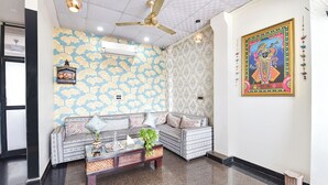 A room with patterned wallpaper, a ceiling fan, a sofa with cushions, a small table with a plant, and a framed picture on the wall. - Fabhotel Down Town (Jaipur)