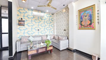 Una habitación con papel tapiz estampado, un ventilador de techo, un sofá con cojines, una mesita con una planta y un cuadro en la pared.
