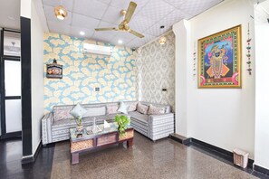 Ein Zimmer mit strukturiertem Wandpapier, einem Deckenventilator, einer Couch mit Kissen, einem kleinen Tisch mit einer Pflanze und einem gerahmten Bild an der Wand.