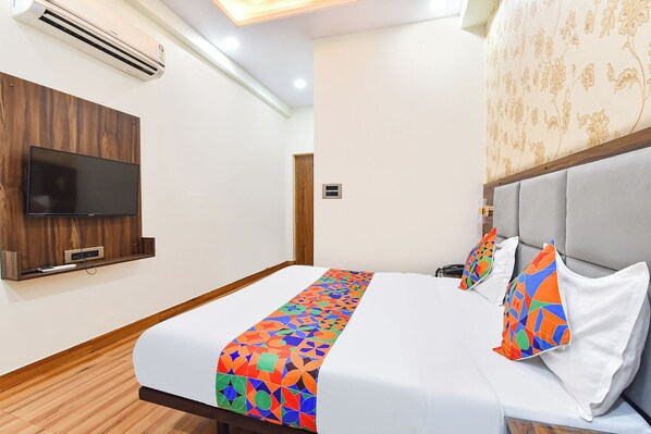 A hotel room with a bed, a television mounted on the wall, and a patterned wallpaper.