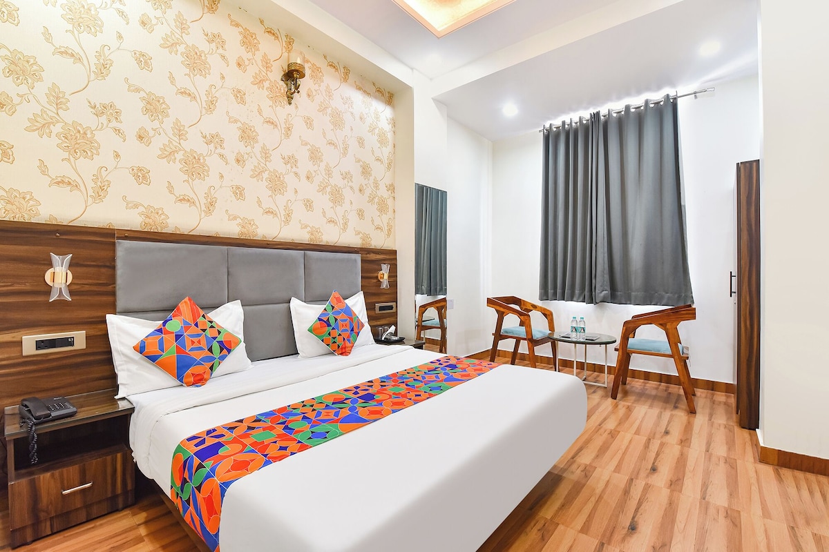 A hotel room with a large bed, a bedside table with a phone, a small table with chairs, and a window with curtains.