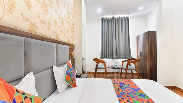 A hotel room with a bed, two chairs, a small table with water bottles, a wardrobe, and a window with curtains. - Fabhotel Down Town (Jaipur)