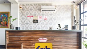 A reception desk with a wooden finish, a reception sign, and a wall-mounted air conditioning unit. - Fabhotel Down Town (Jaipur)
