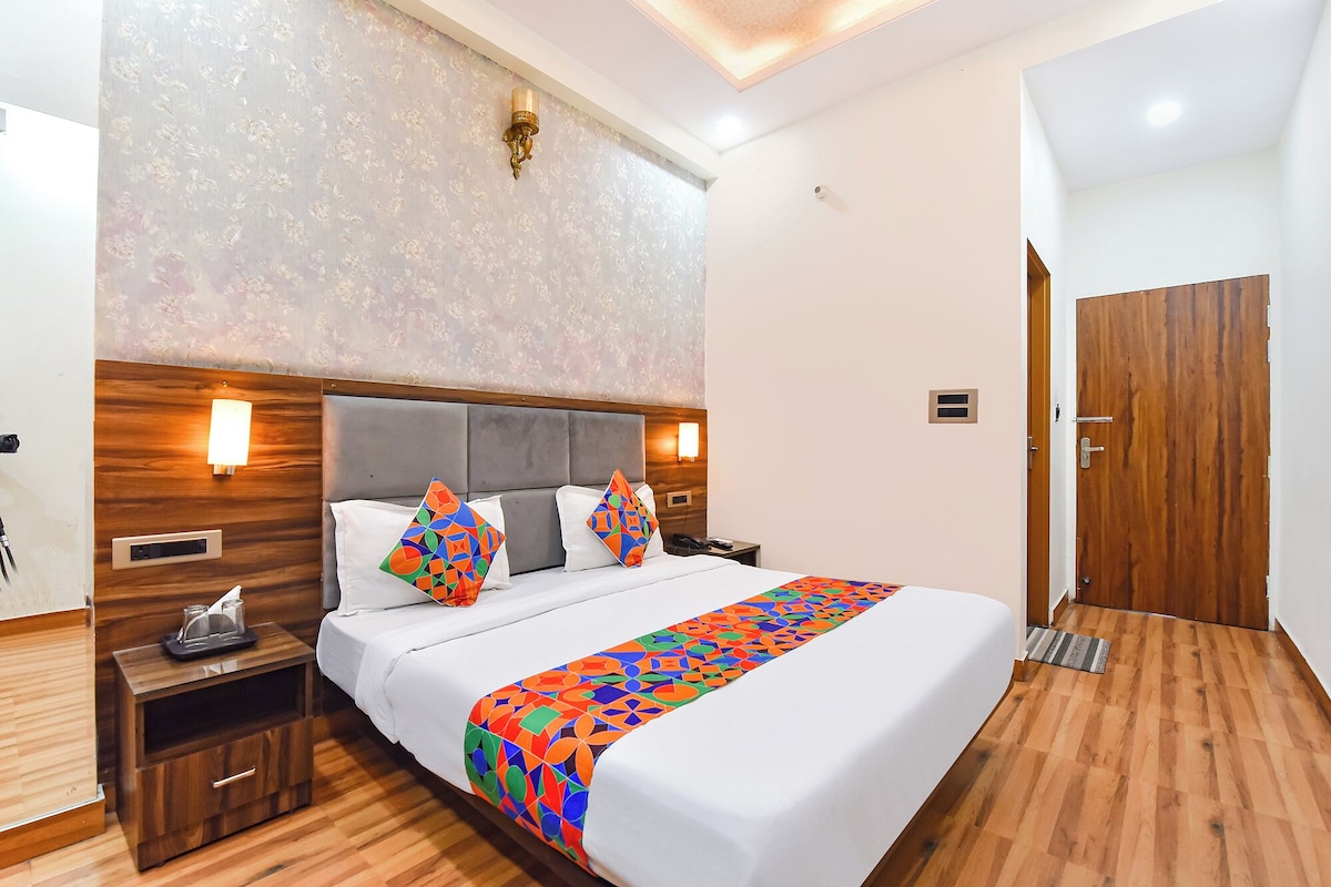 A hotel room with a bed, bedside tables, a nightstand, a wooden wardrobe, a wall-mounted light fixture, and a door.