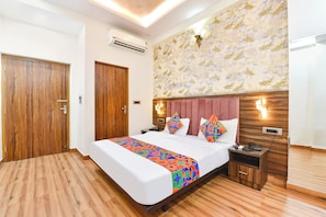 A hotel room with a large bed, a wooden wardrobe, a nightstand, and a wall-mounted air conditioner. - Fabhotel Down Town (Jaipur)