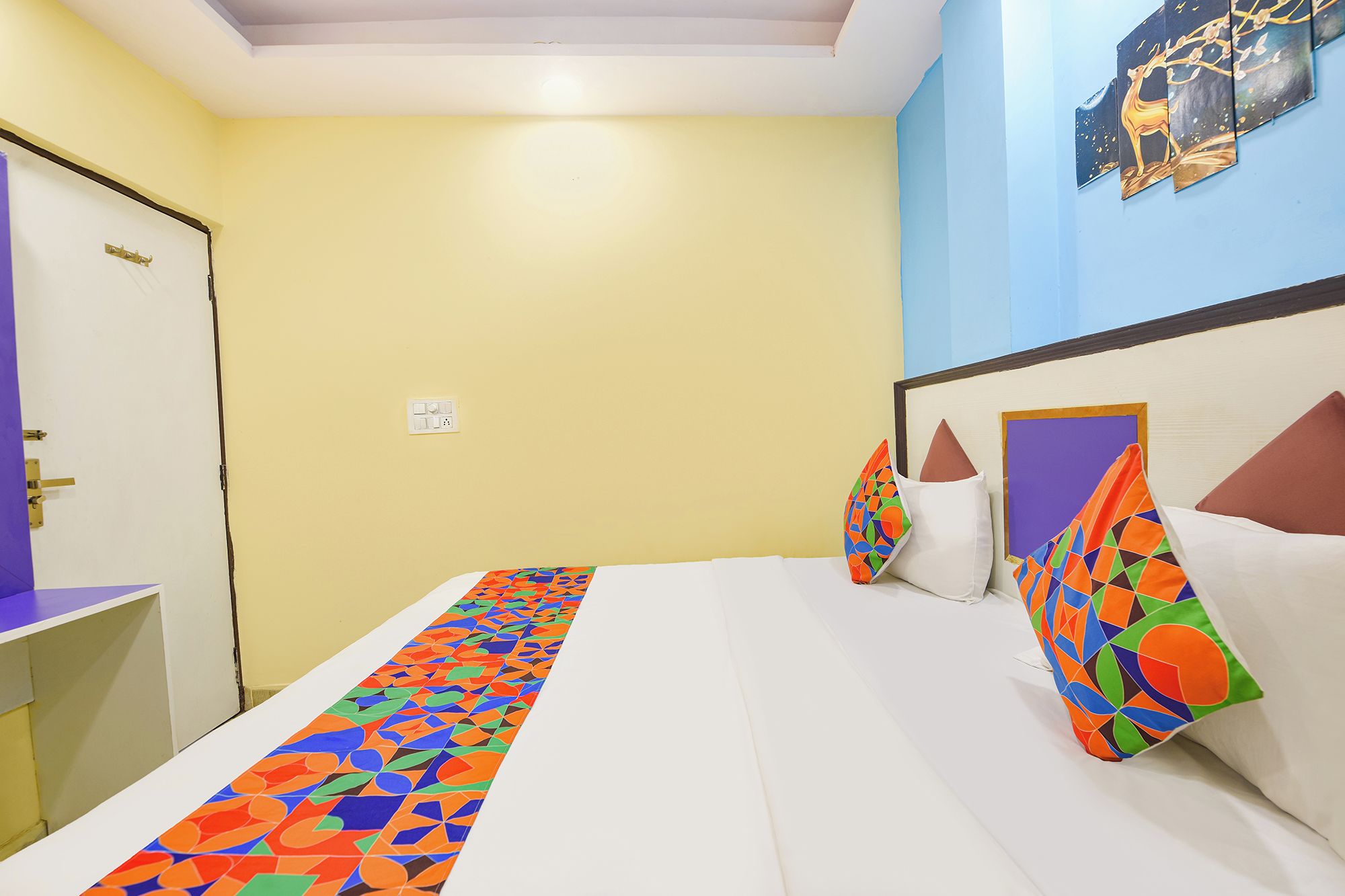 A hotel room with a bed, pillows, a bedside table, and a wall with artwork.