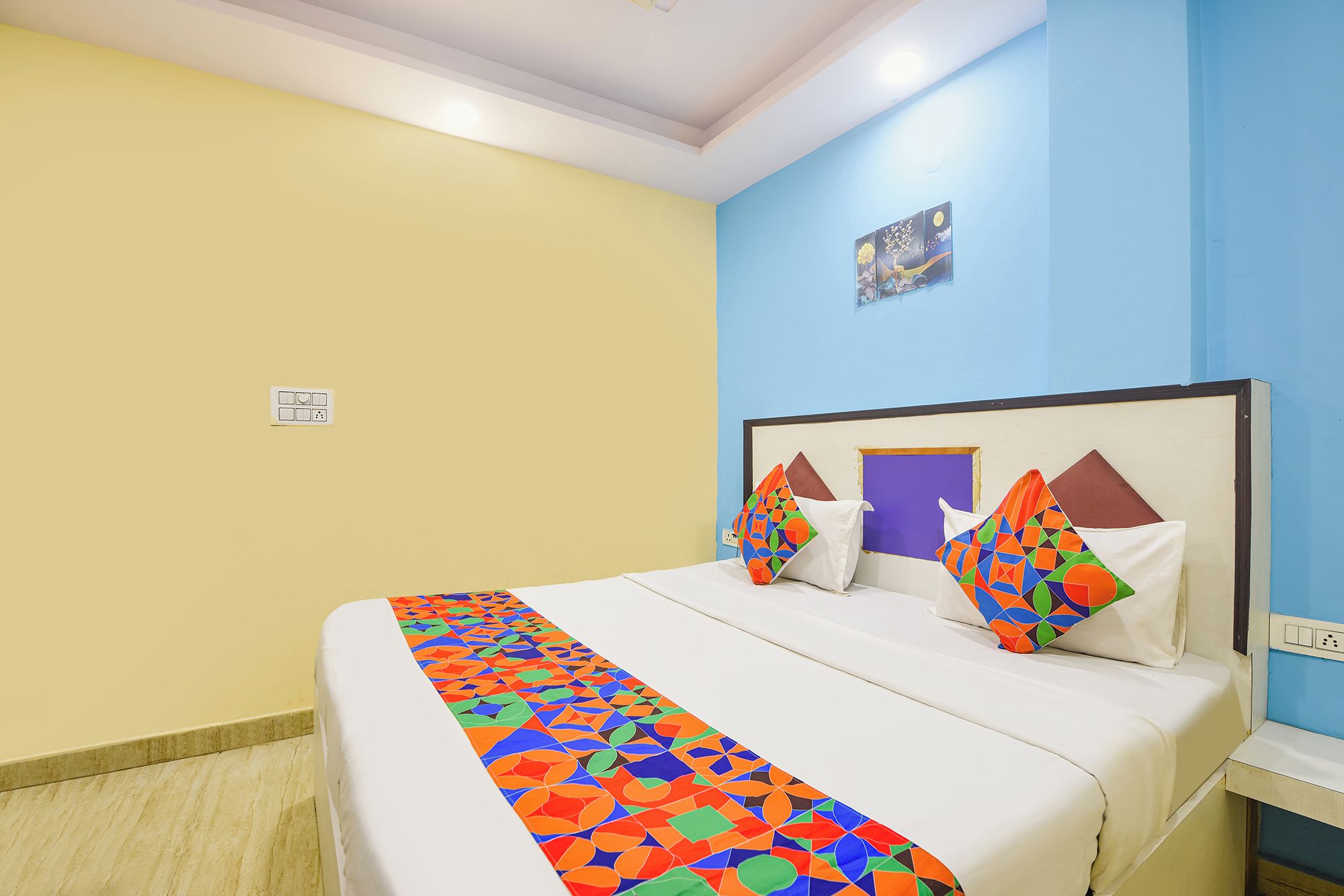 Una habitación de hotel con una cama, una mesita de noche y un cuadro en la pared.
