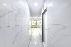 Un passadís amb parets de marbre blanc i un sòl polit que condueix a una porta amb un senyal vermell.
