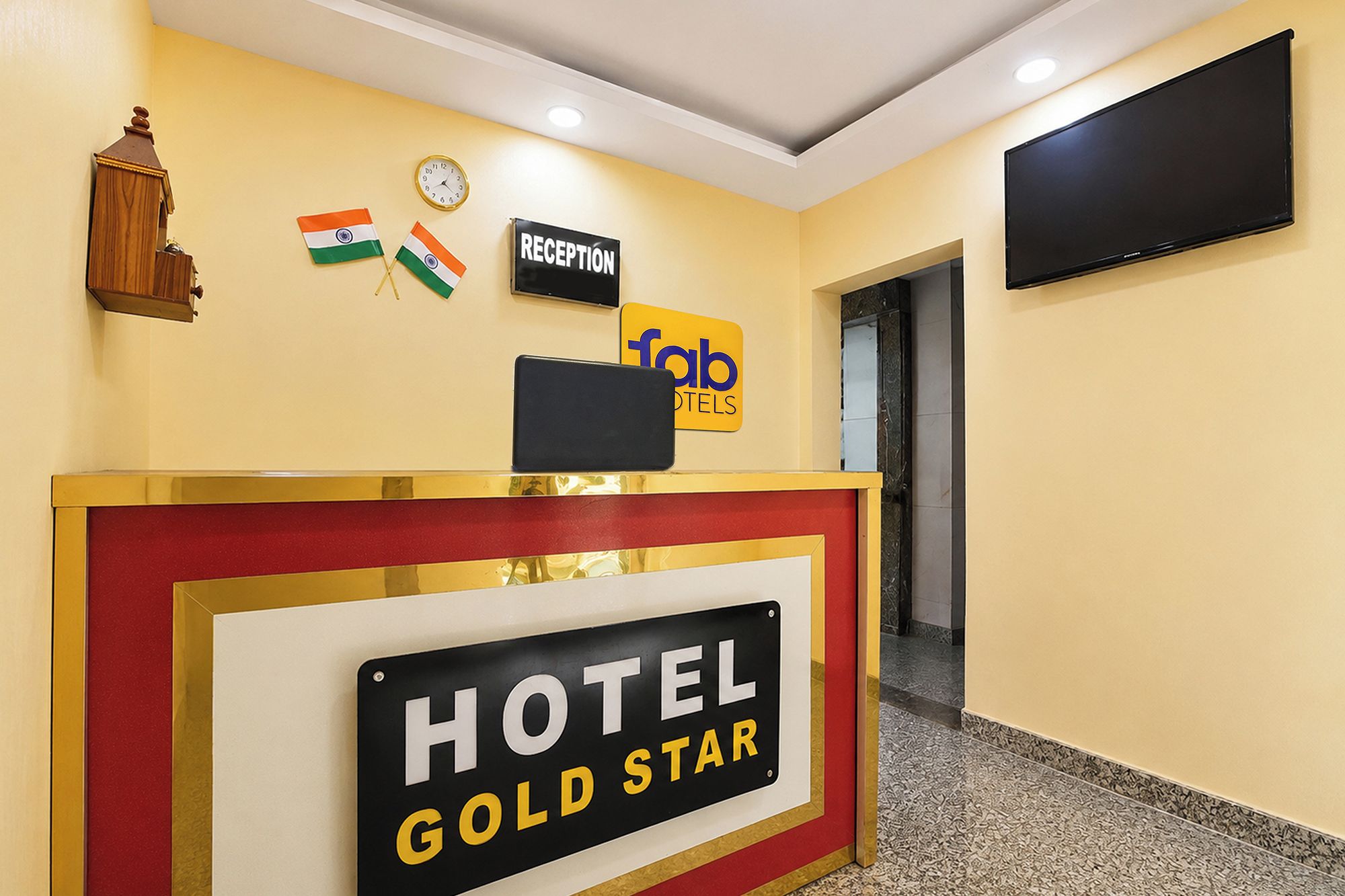 Un comptoir d’accueil d’hôtel avec une enseigne indiquant « HÔTEL GOLD STAR », une horloge et deux drapeaux.