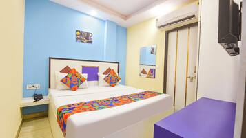 A hotel room with a bed, bedside table, and a purple bench.