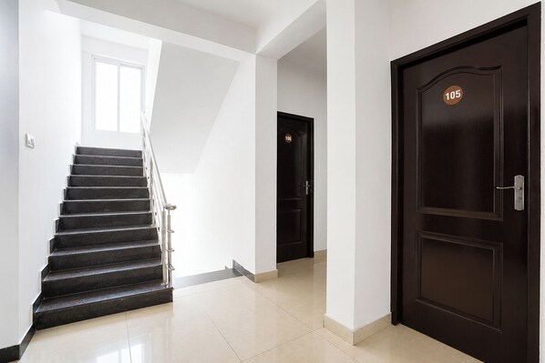 A staircase leading to a door with a number plate, a light-colored tiled floor, and a white wall.