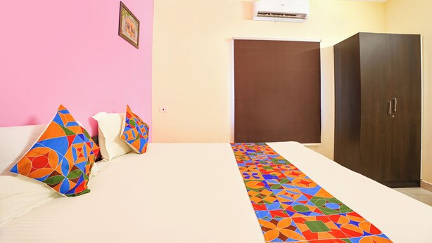A hotel room with a bed, pillows, a wardrobe, and an air conditioning unit.