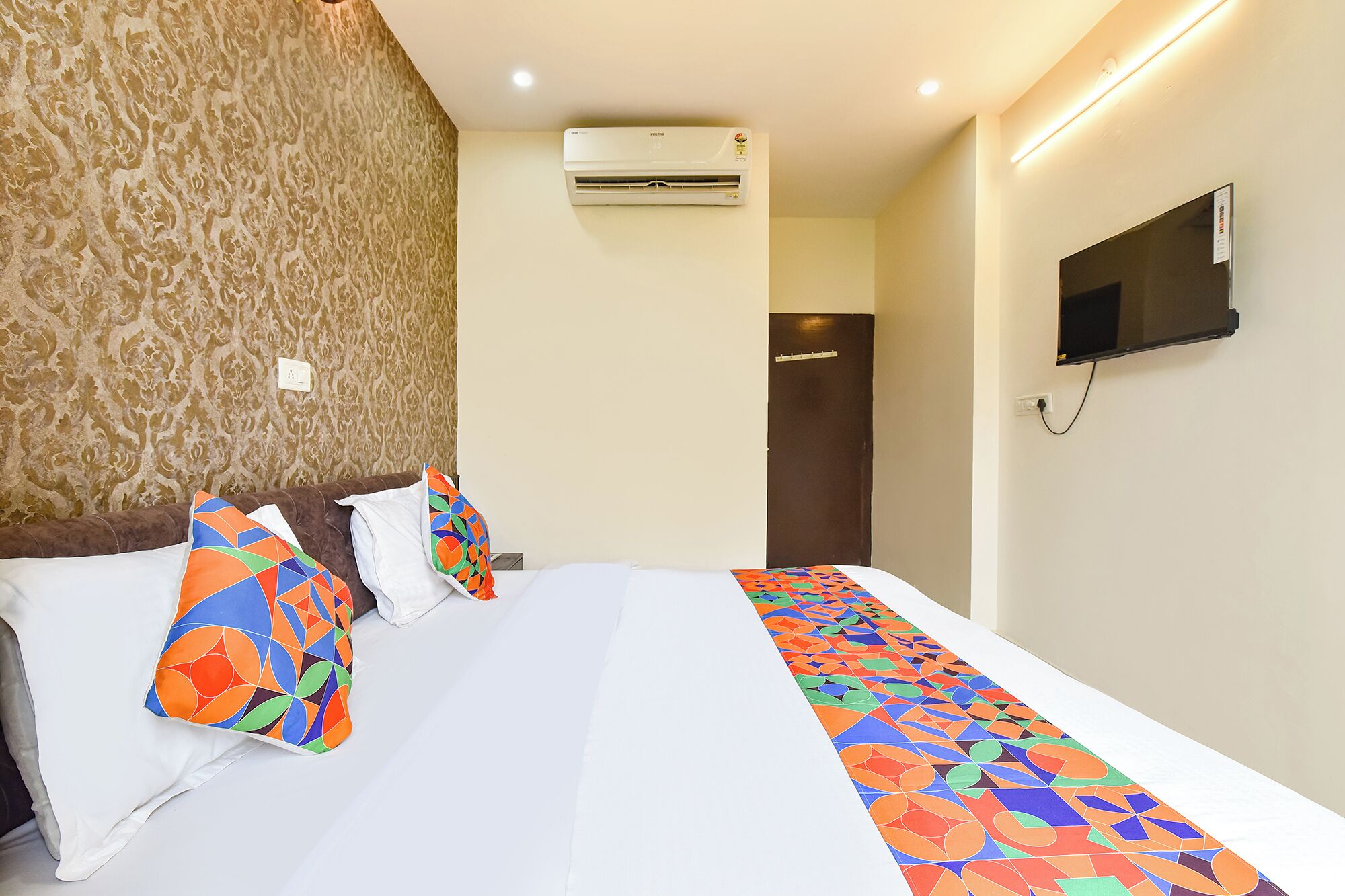 Una habitación de hotel con una cama, un televisor montado en la pared y un equipo de aire acondicionado.