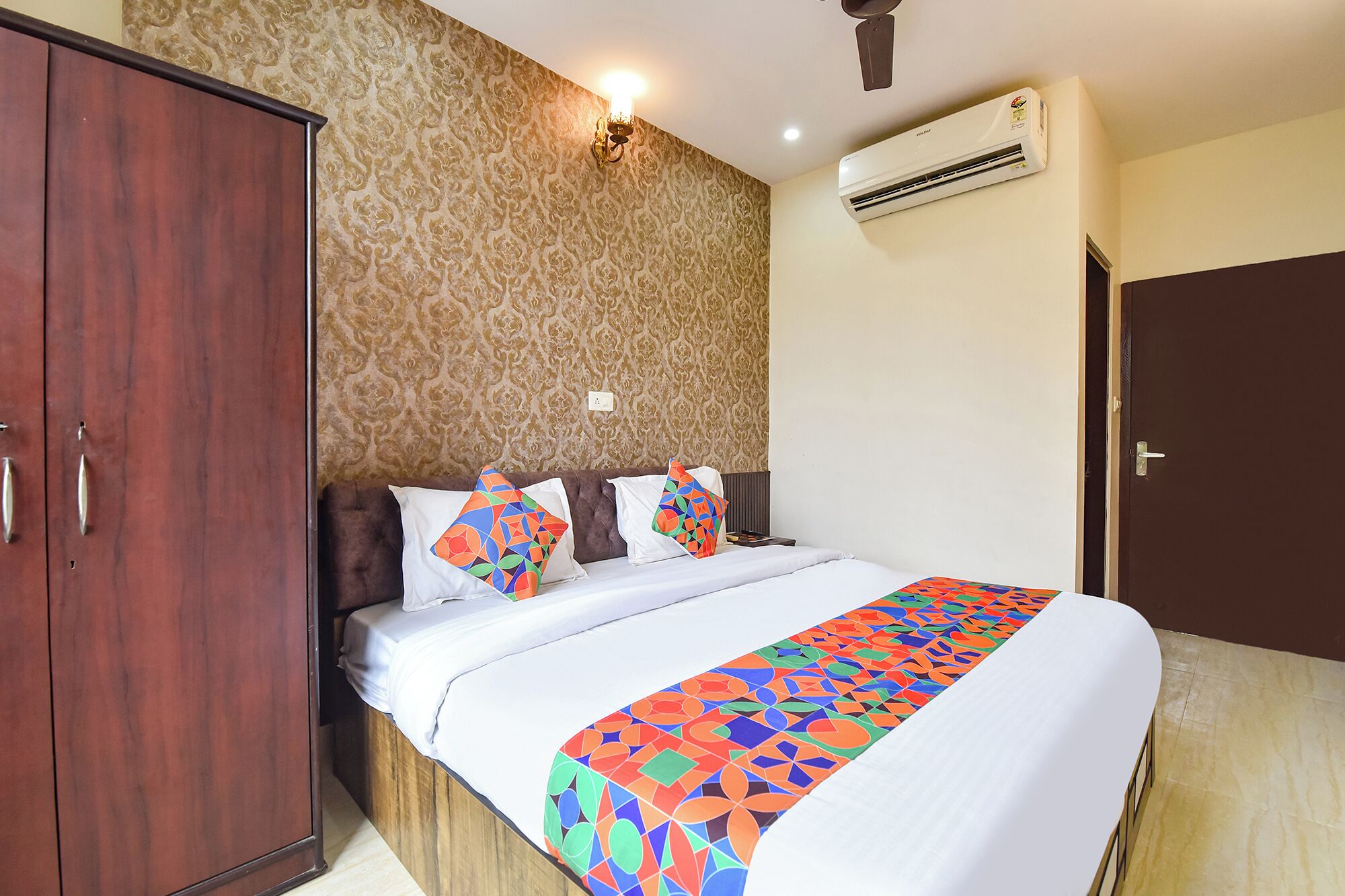 A hotel room with a bed, a wardrobe, an air conditioning unit, and a patterned wallpaper.